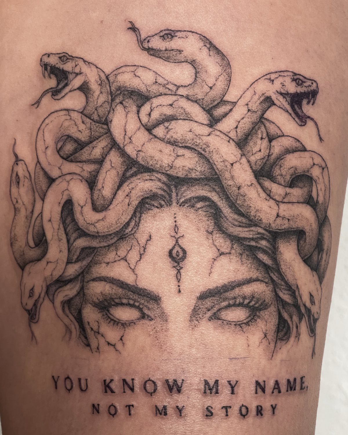 Medusa tattoo with snakes for hair and text on a person's skin