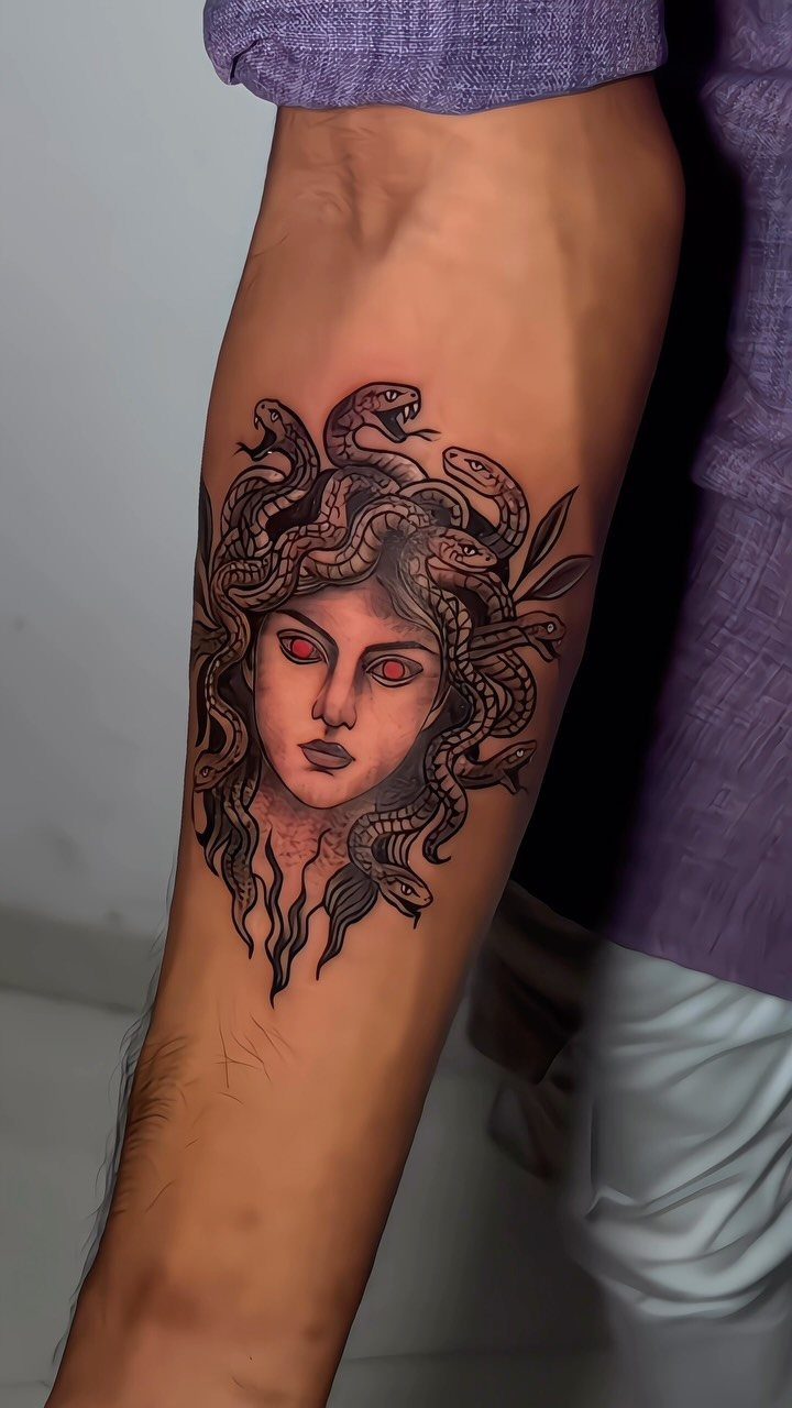 Medusa tattoo on a forearm featuring a woman with red eyes and snake hair.
