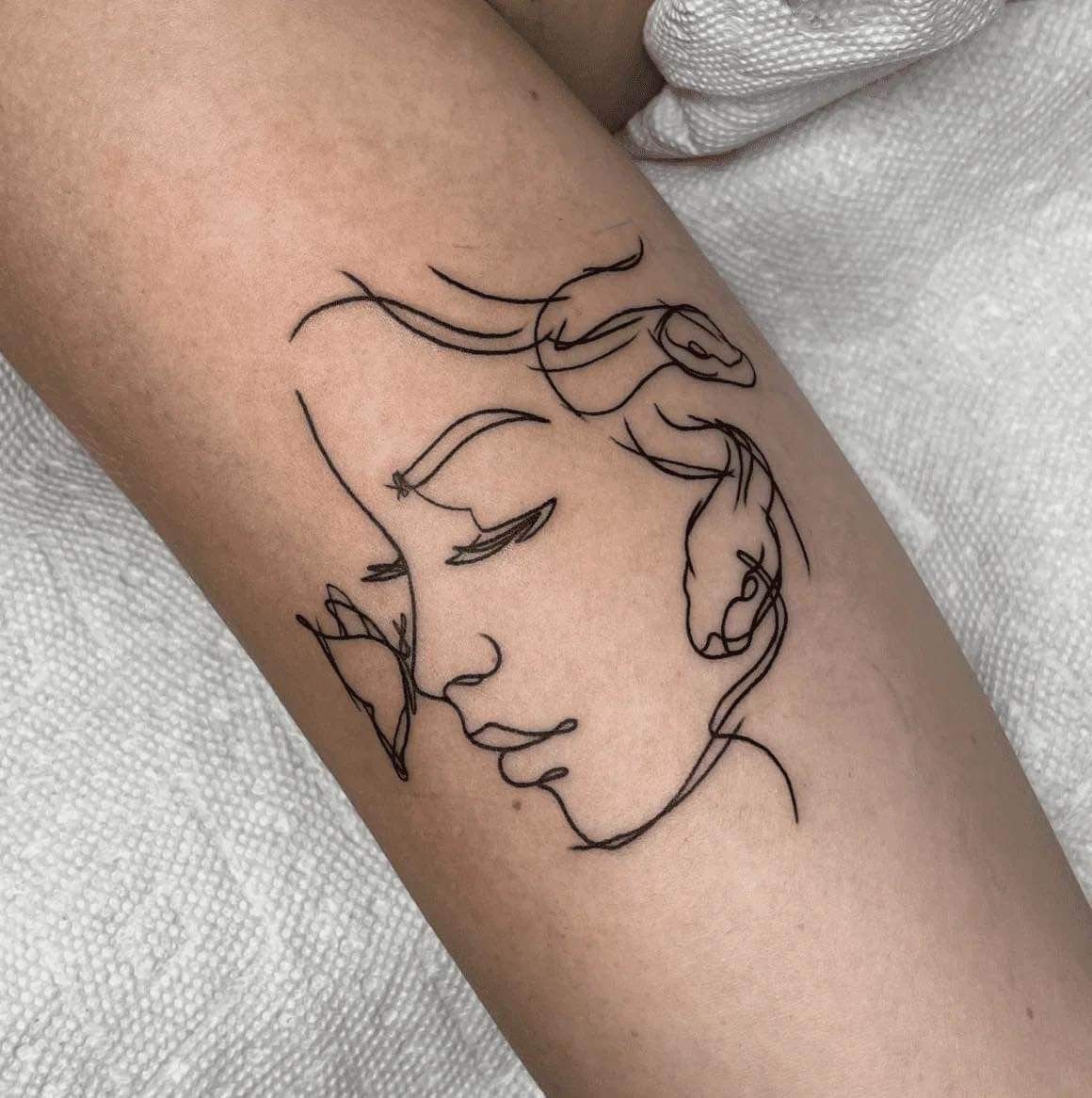 Minimalist Medusa outline tattoo on an arm featuring a feminine profile with snake hair.