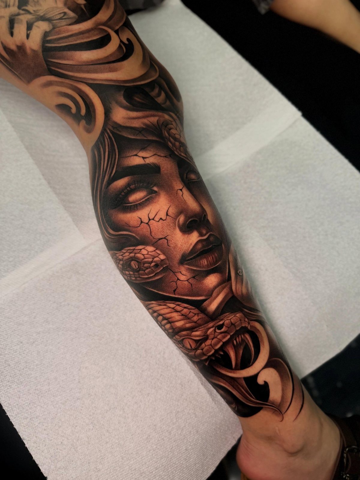 Medusa tattoo on a forearm featuring a cracked face and realistic snakes.