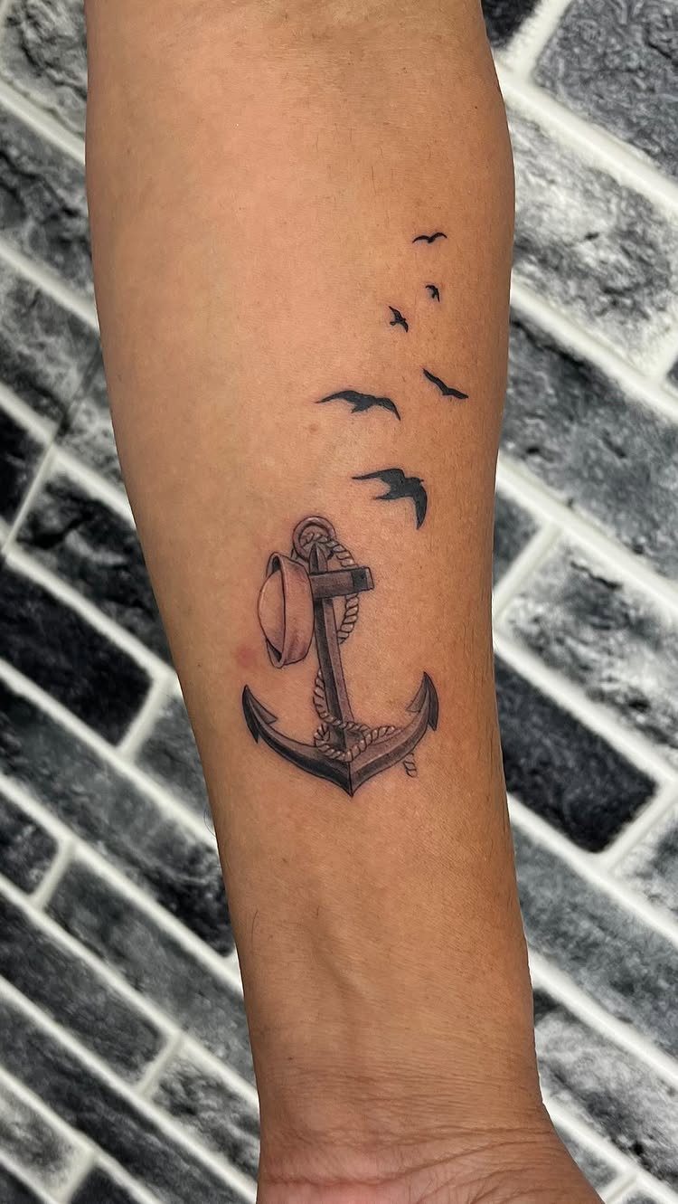Anchor tattoo with flying birds on a forearm against a brick wall background
