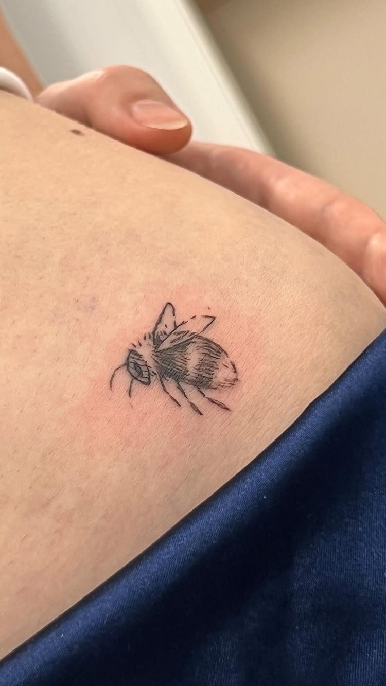 Small black ink bumblebee tattoo on a person's fair skin.