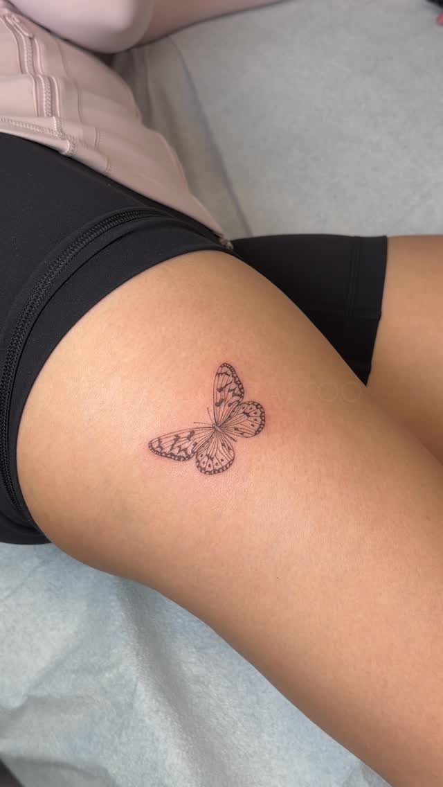 Small black ink butterfly tattoo on a person's upper thigh