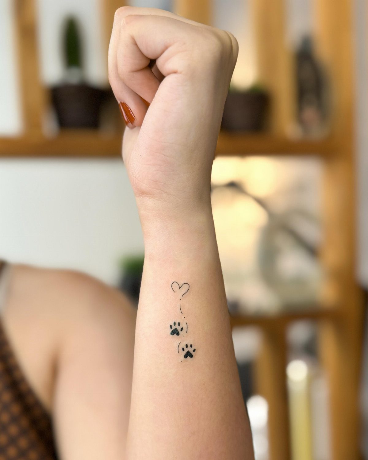 Small black heart and dog paw print tattoos on a person's inner wrist.