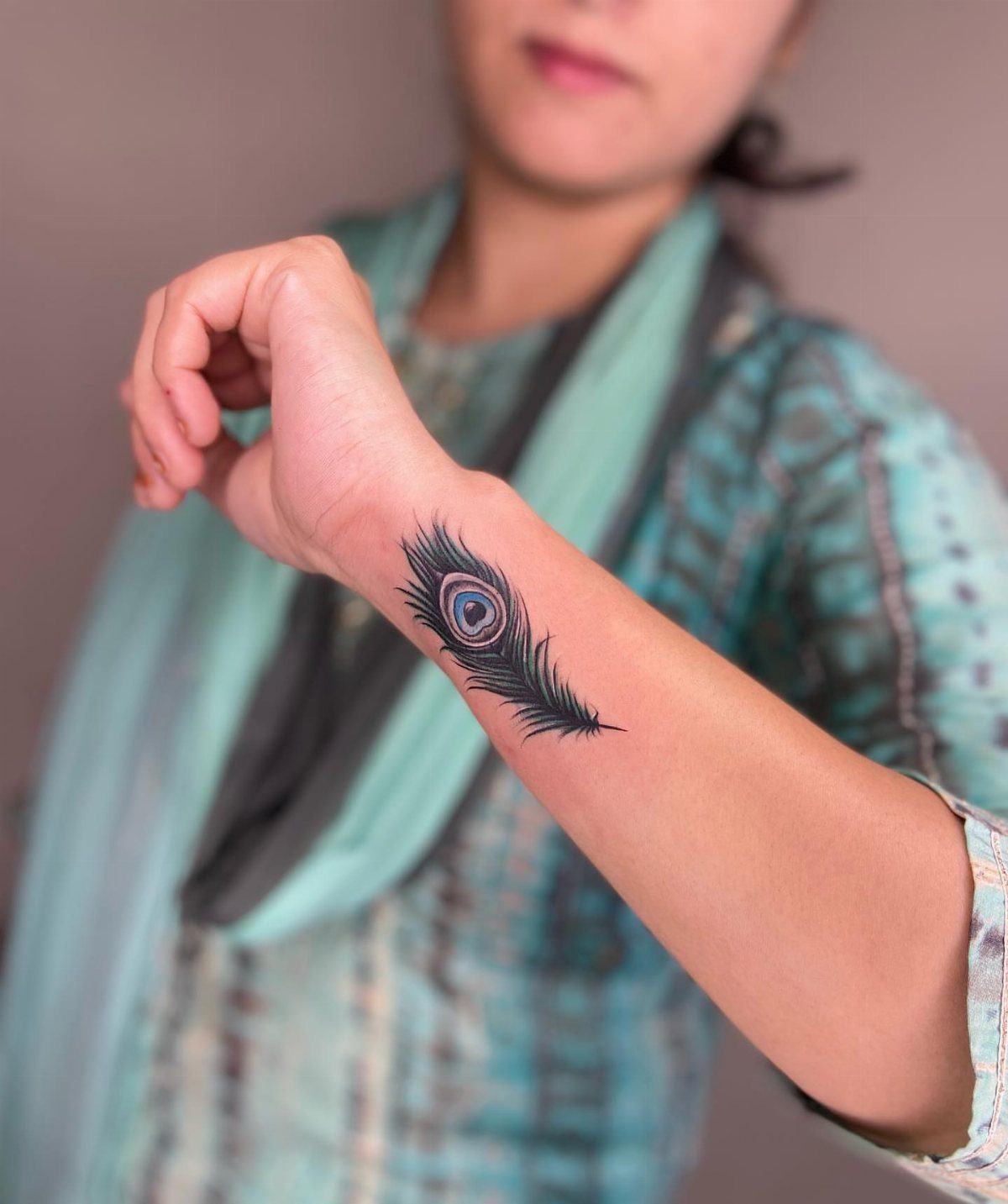 Peacock feather tattoo on a person's inner forearm with blue and black ink.