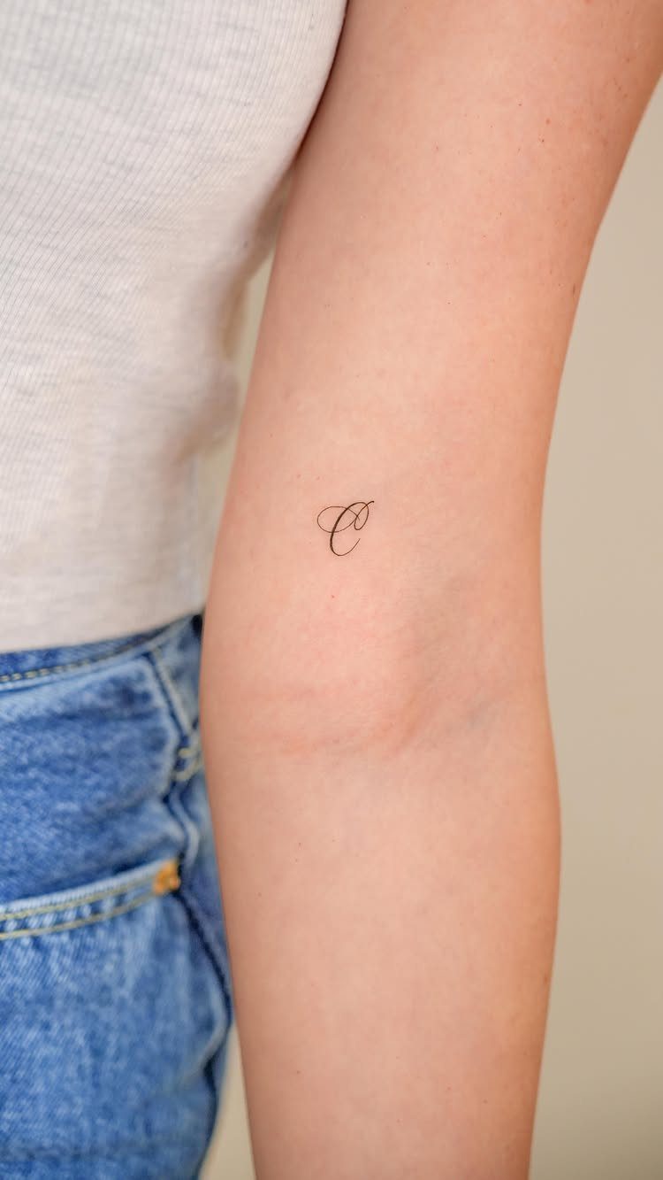 Cursive letter C tattoo on the inner arm of a person