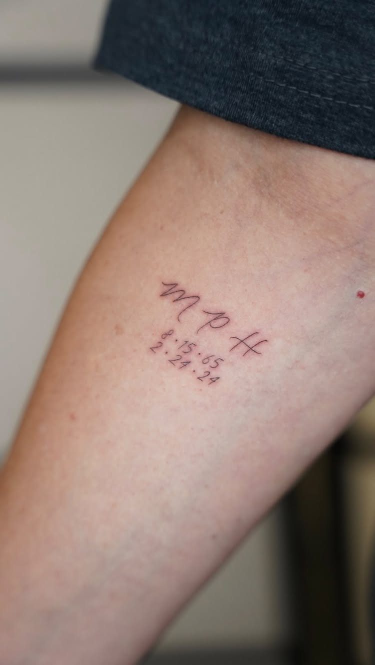 Small red ink tattoo of initials and dates on a person's forearm