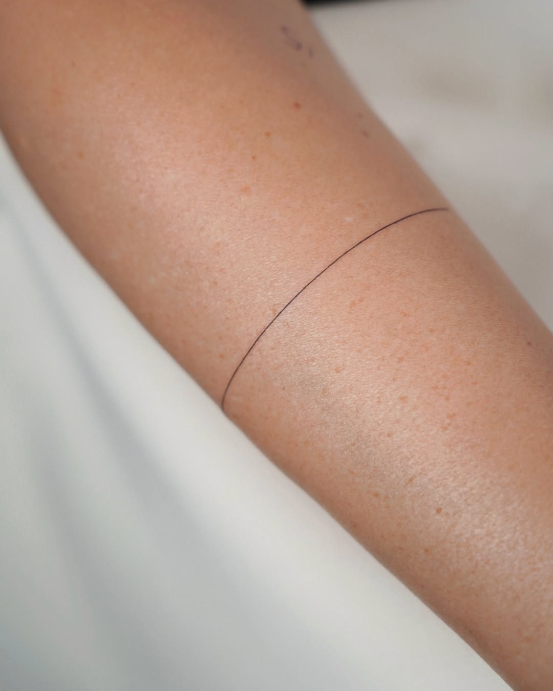 Thin black minimalist line tattoo wrapping around a person's fair-skinned forearm.