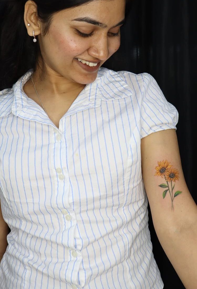 Woman with a colorful tattoo of two yellow sunflowers on her upper arm.