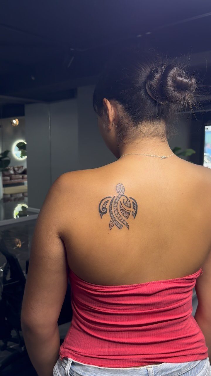 Sea turtle tattoo on the upper back shoulder of a woman in red.