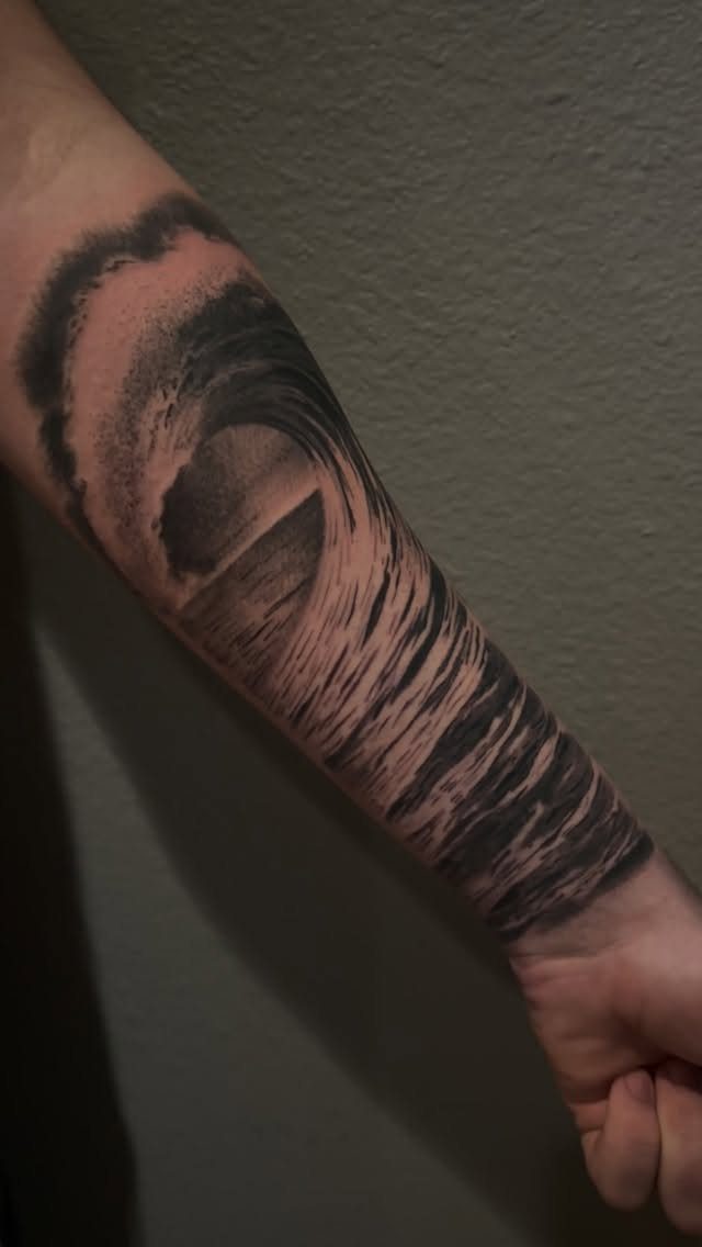 Black and grey ocean wave tattoo on a person's forearm.