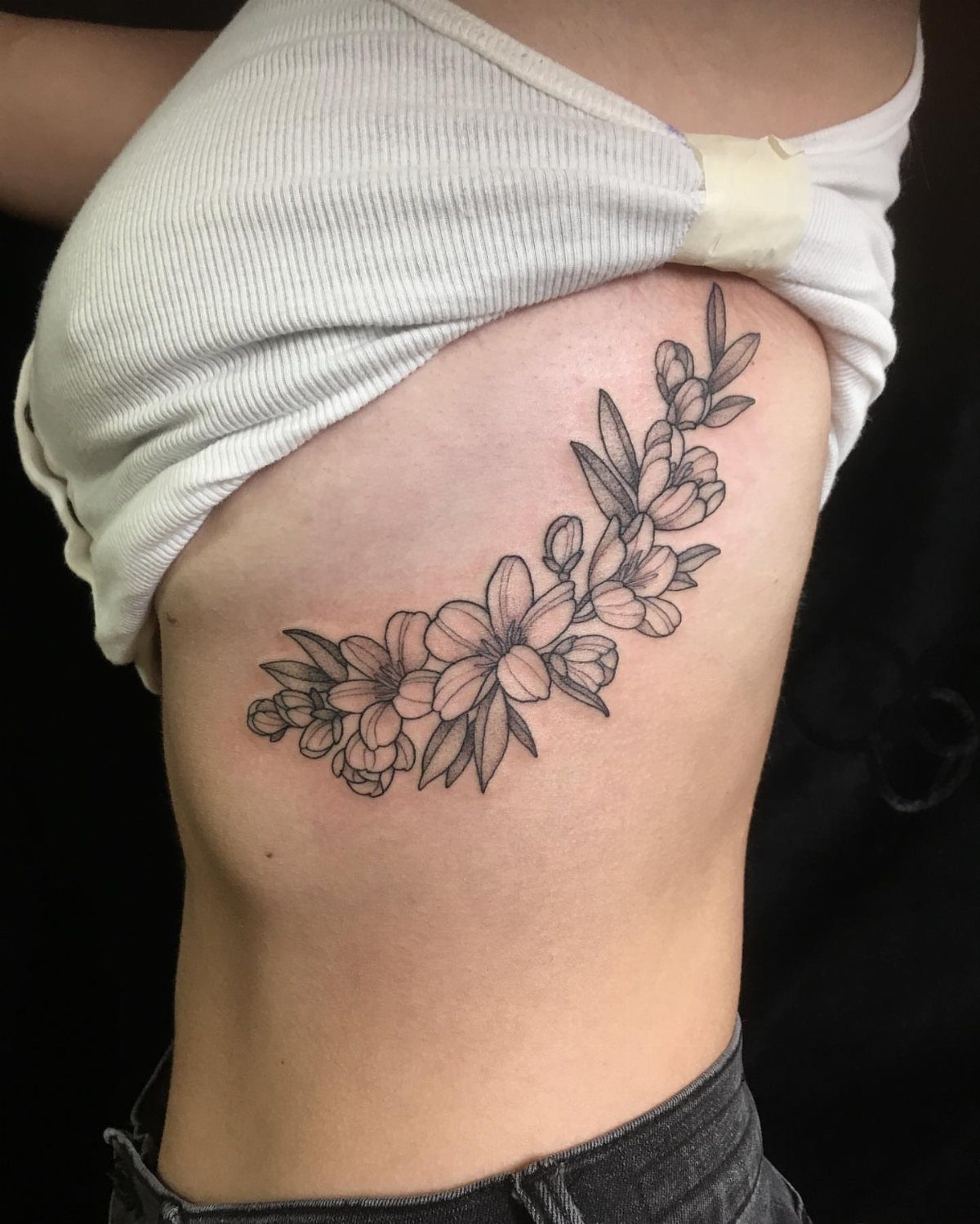 Cherry blossom branch tattoo in black ink on a person's ribcage