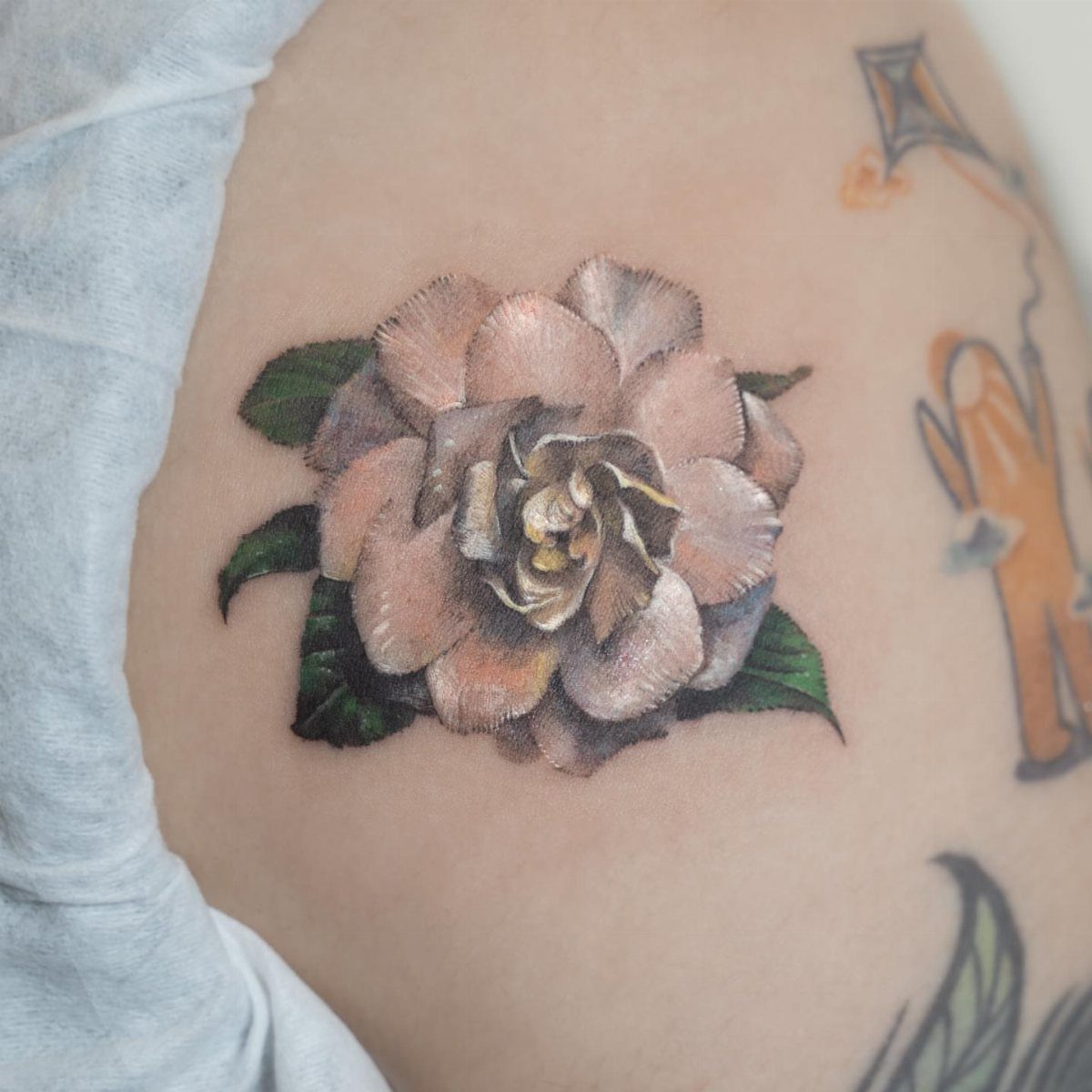 White gardenia flower tattoo with green leaves on a person's ribcage.