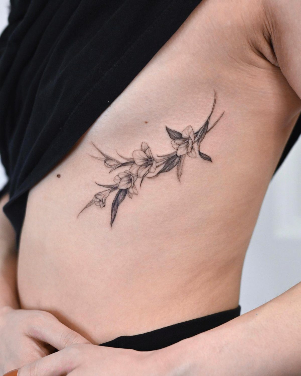 Floral spray tattoo with delicate flowers and leaves on a person's ribcage.