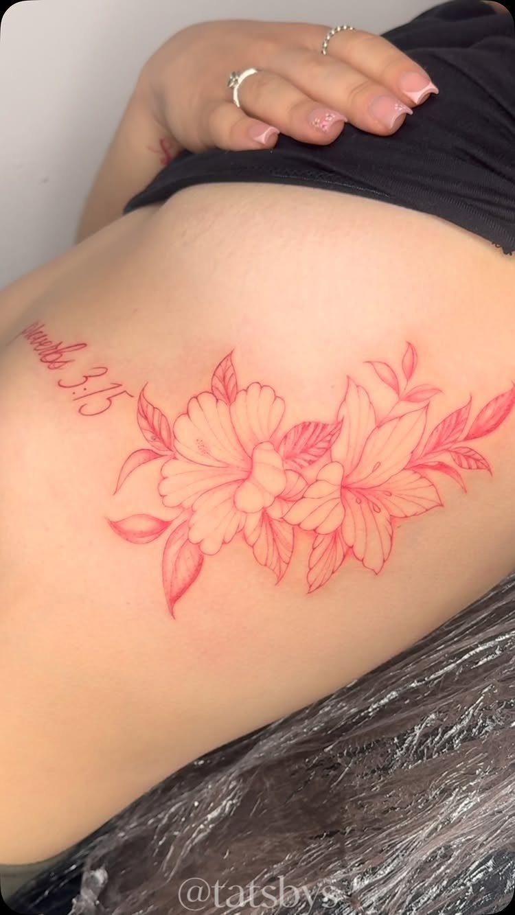 Two red hibiscus flowers tattooed on a woman's ribcage with accompanying script text.