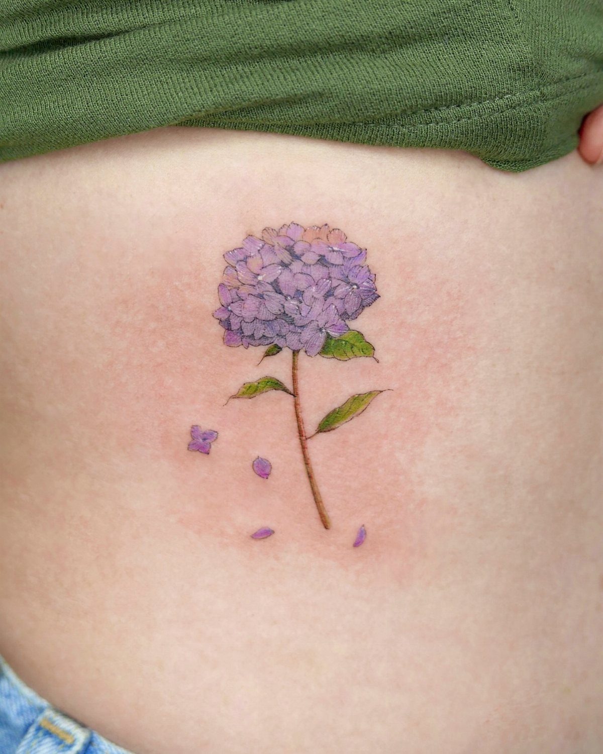 Purple hydrangea flower tattoo with green stem on a person's ribcage
