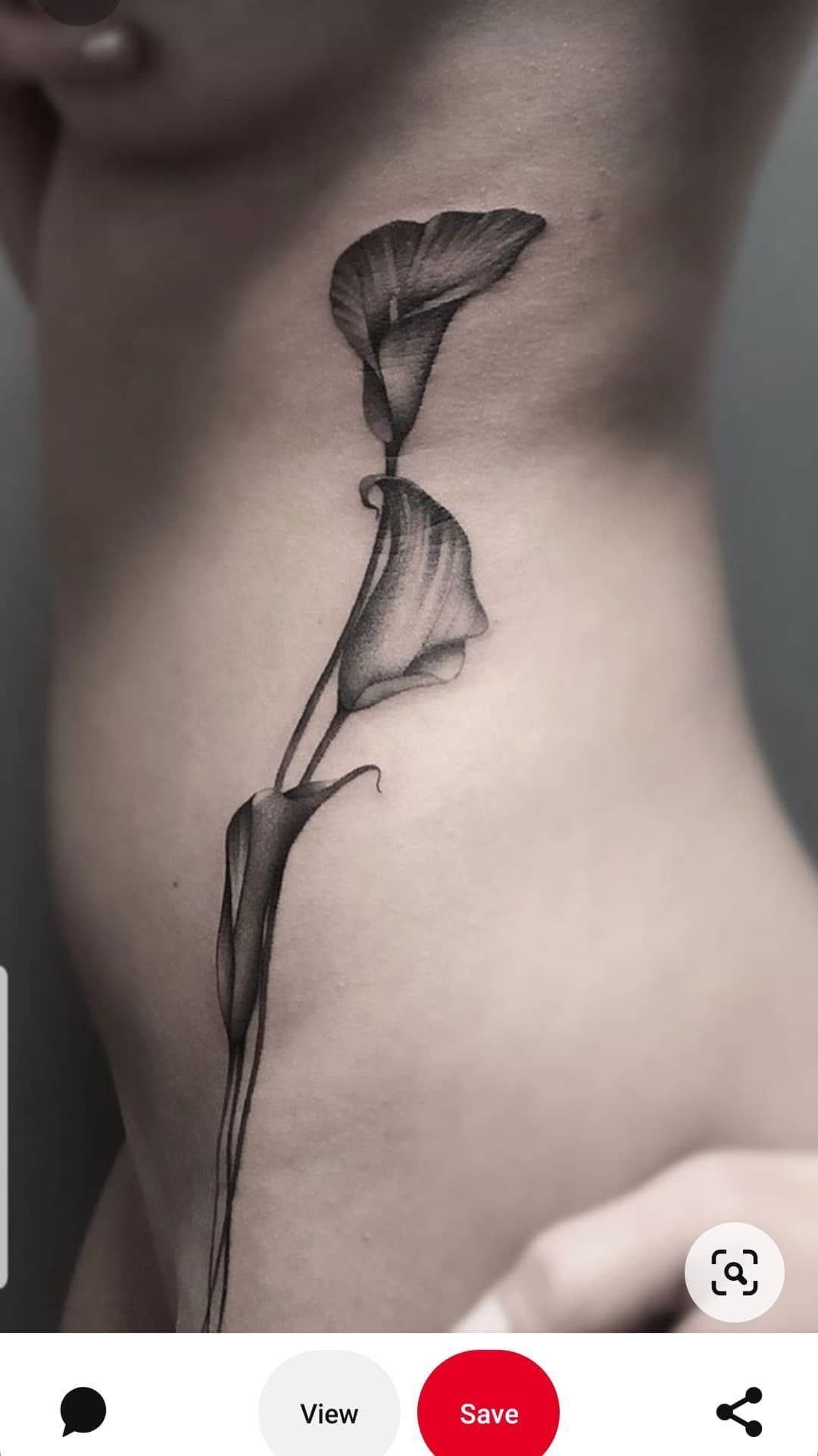 Calla lily flower tattoo with long stems on a person's ribcage in black ink.