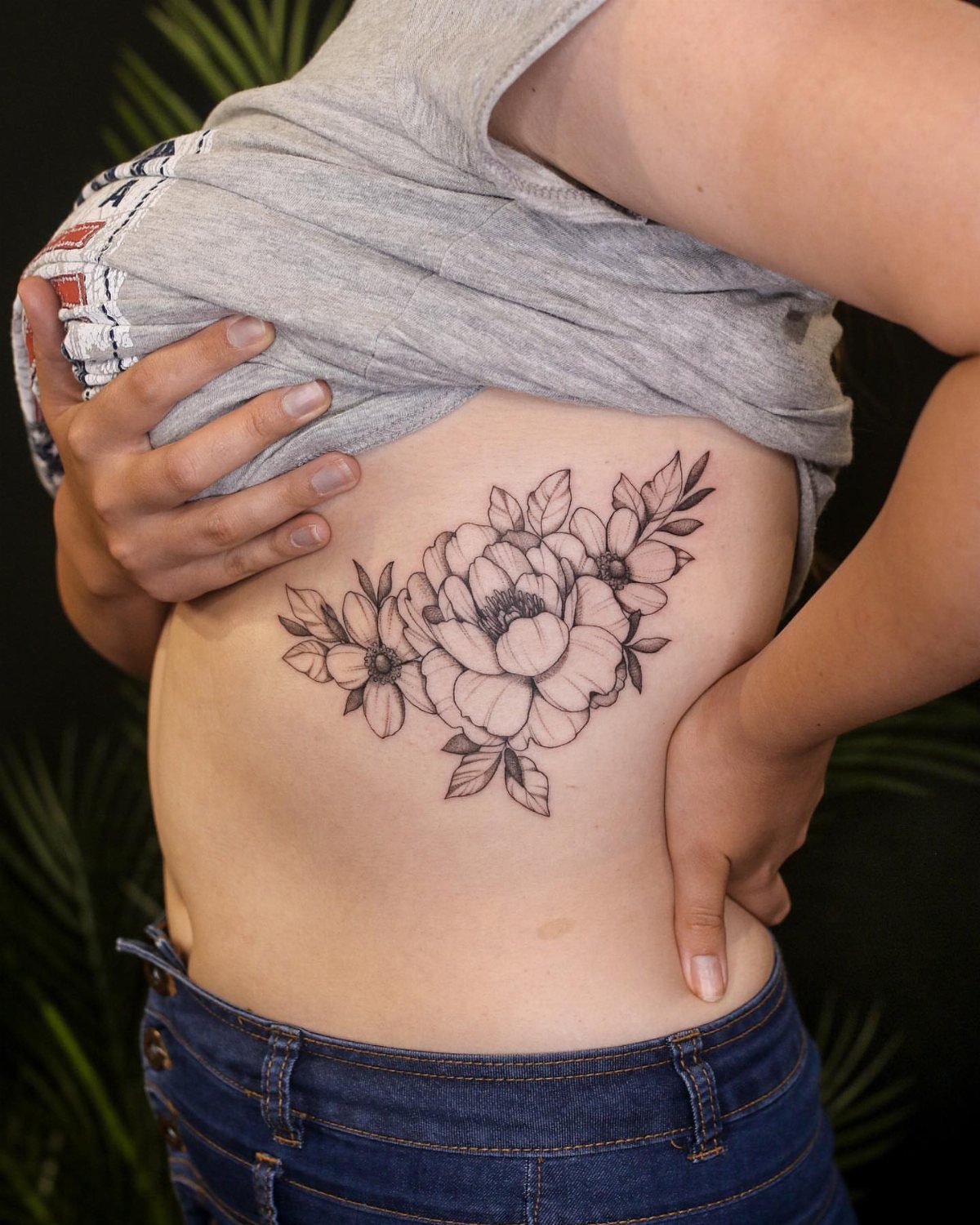 Peony trio flower tattoo in black ink on a woman's ribcage area.