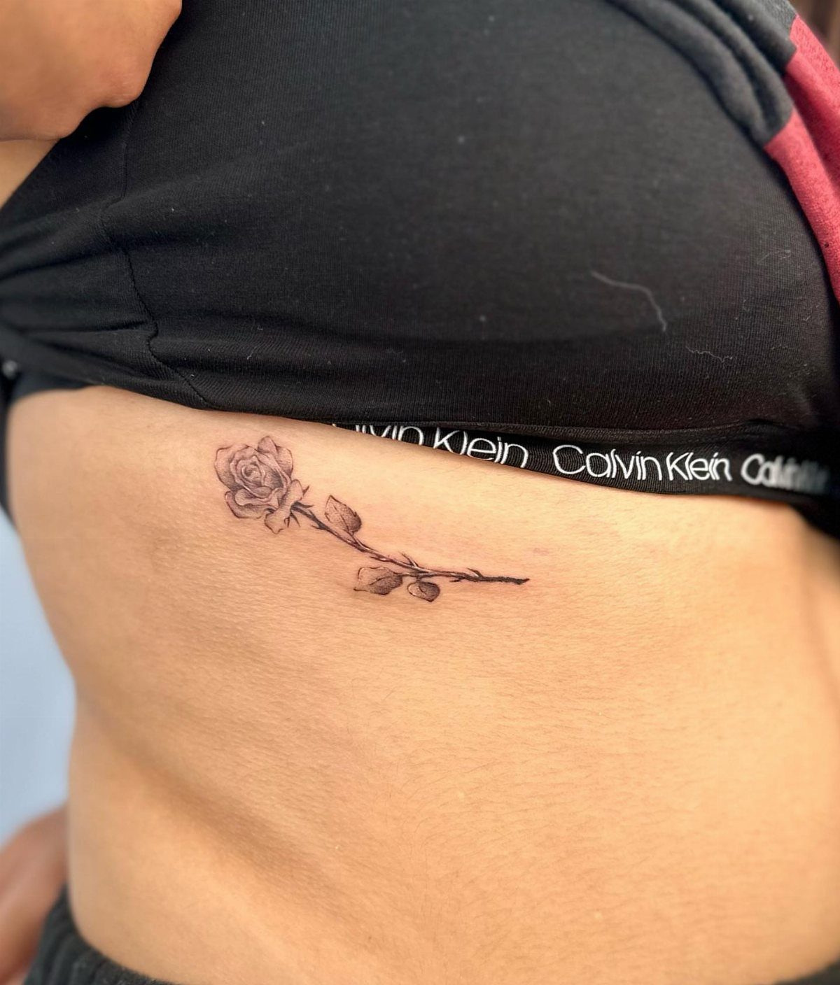 Single rose tattoo with stem and leaves on a person's ribcage area.