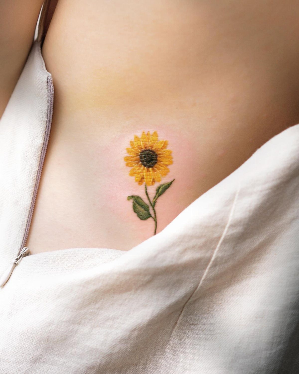 Single yellow sunflower tattoo with green stem on a person's ribcage.