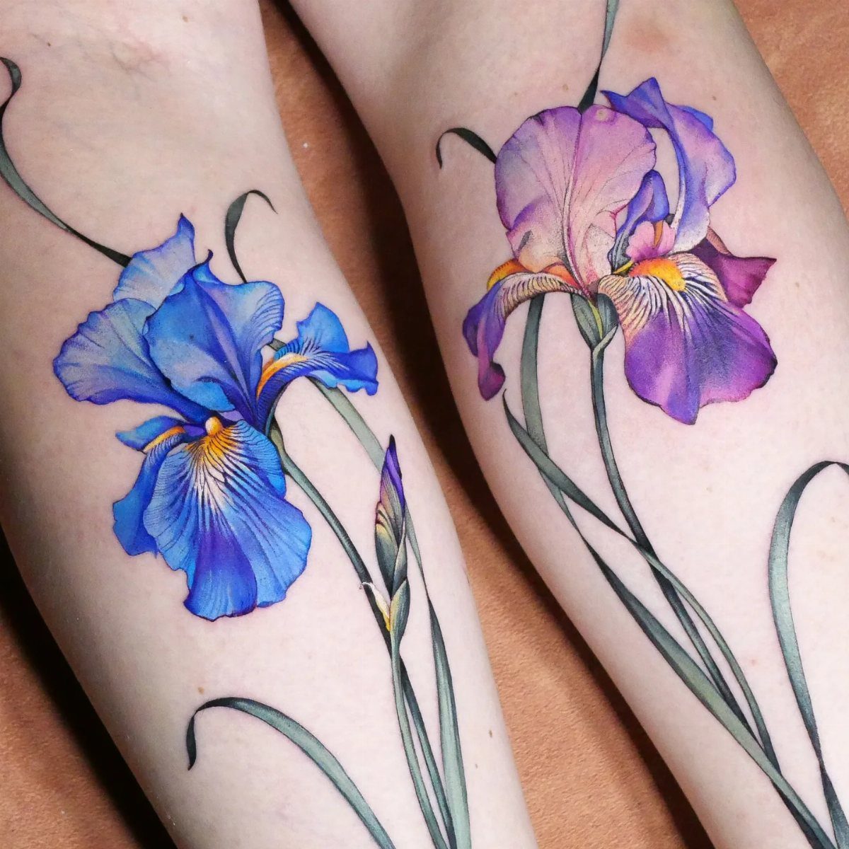 Blue and purple iris flower tattoos with green stems on skin.