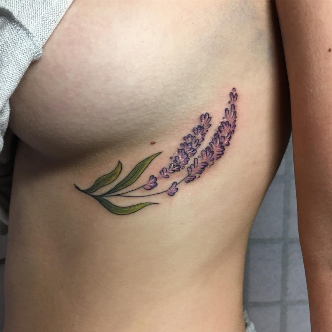 Trailing lavender flower tattoo with purple blooms and green leaves on a woman's ribs.