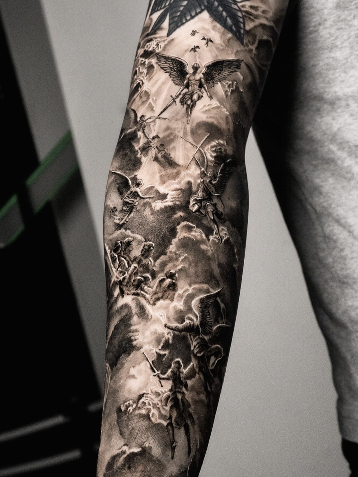 Detailed black and grey sleeve tattoo featuring winged angels among dramatic clouds.