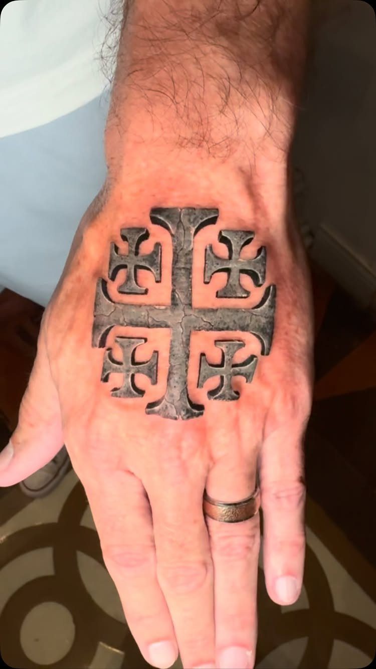 Ornate stone-textured cross tattoo on the back of a person's hand