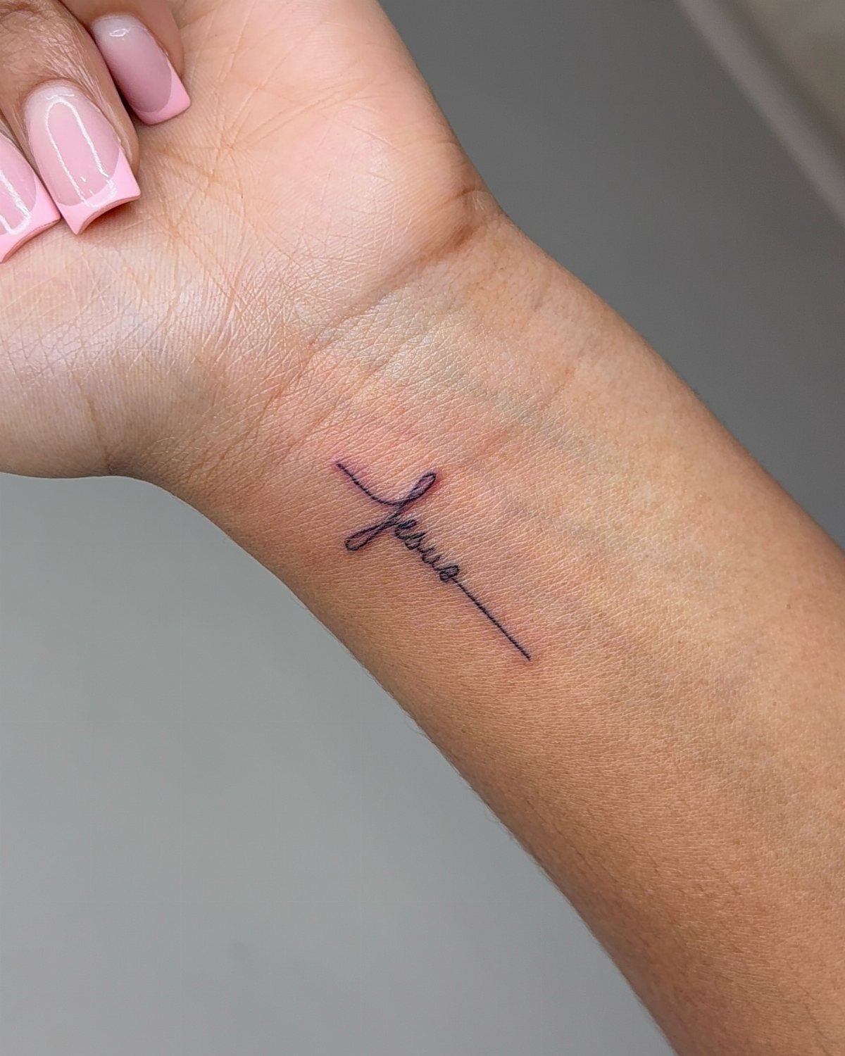 Cursive tattoo of the word Jesus on a person's inner wrist