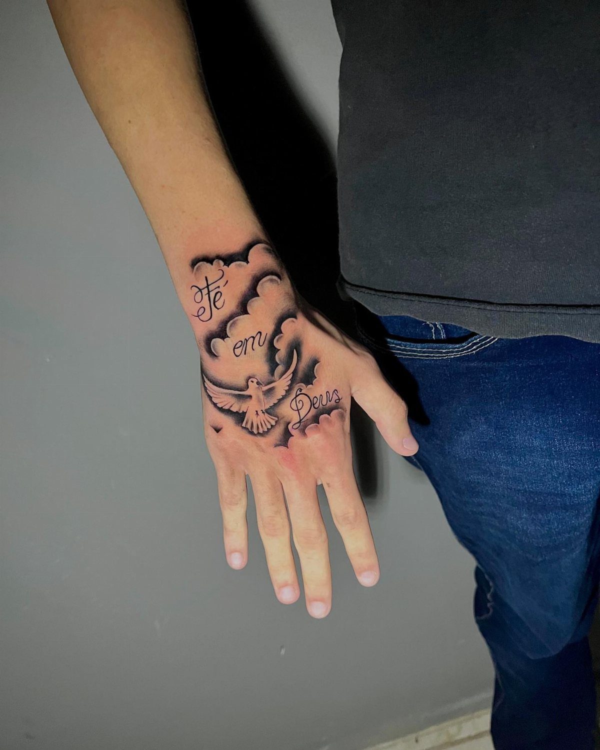 Dove tattoo with clouds and cursive text on a person's hand and wrist.