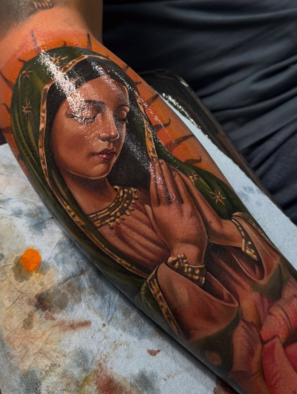 Colorful tattoo of the Virgin Mary with a green cloak and golden halo.