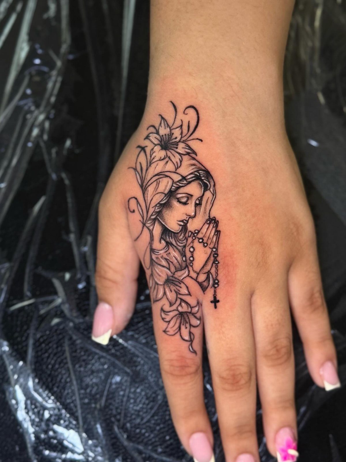 Virgin Mary tattoo in black line art on the back of a hand