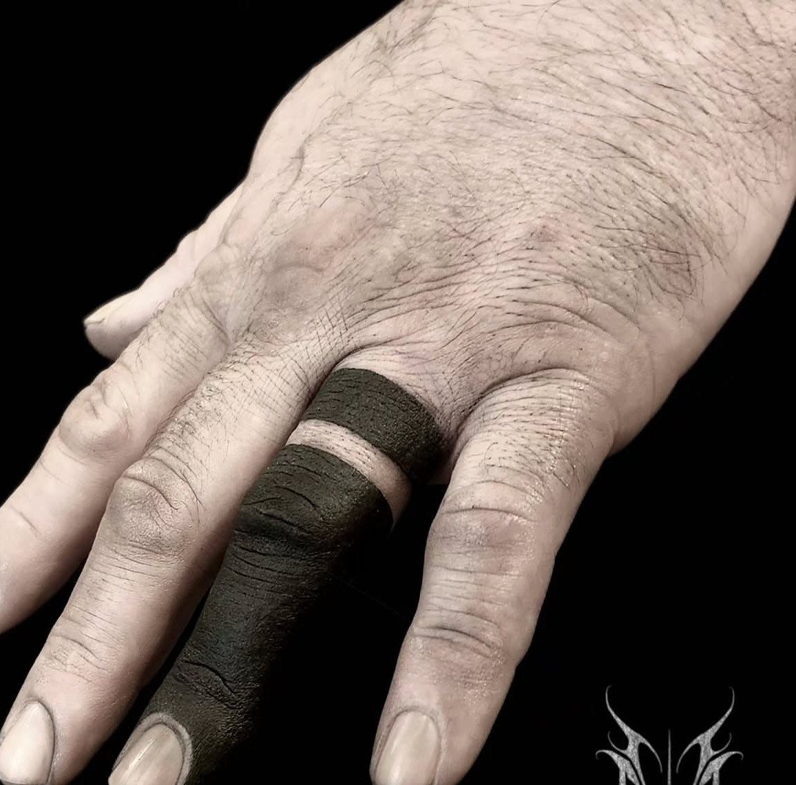 Hand with heavy black ink tattoos covering the index finger and knuckle area.