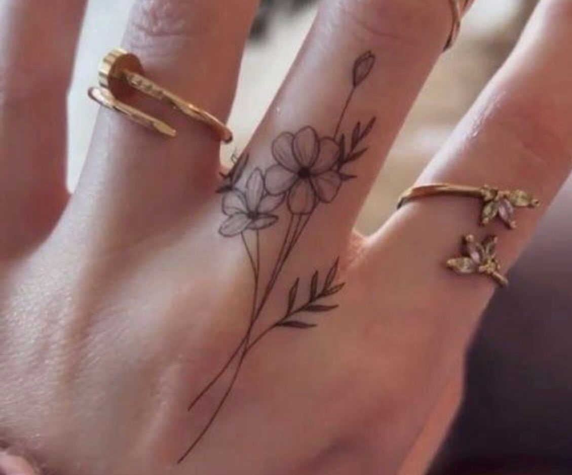 Hand and middle finger with a delicate black ink floral tattoo and gold rings