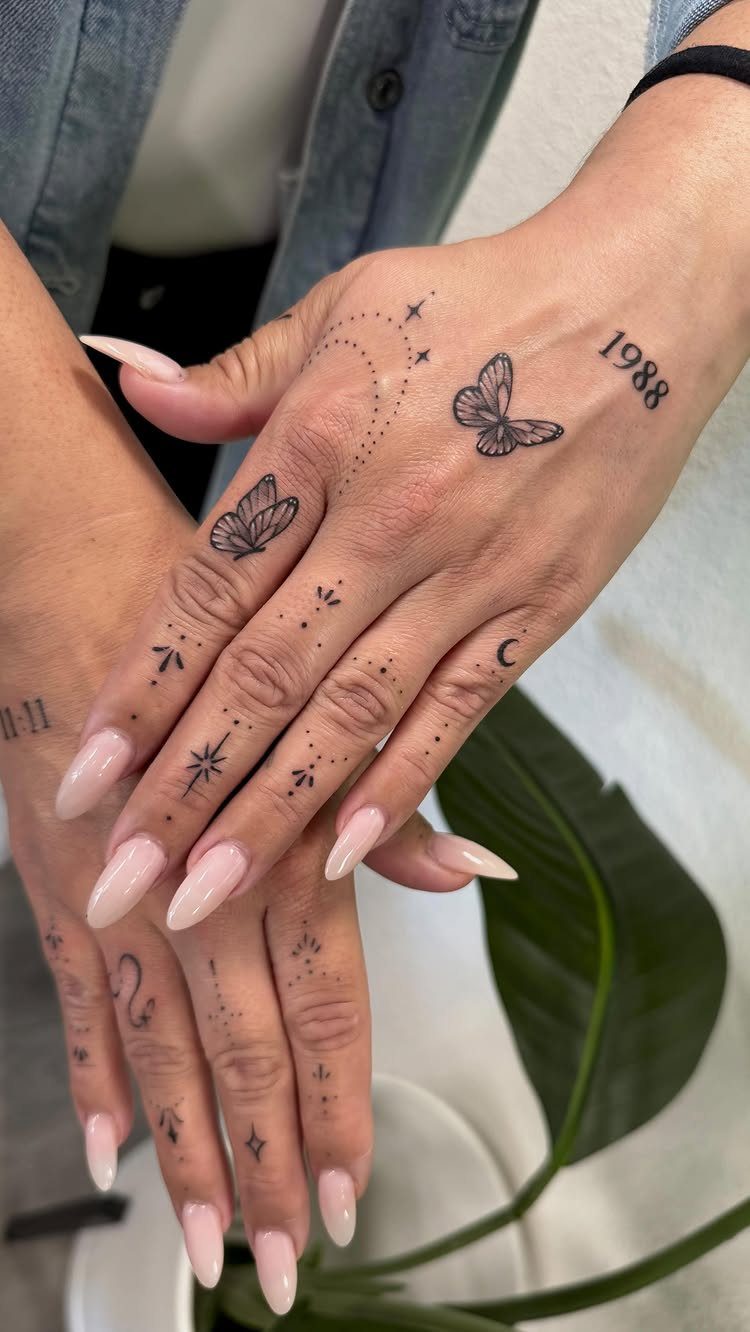 Hands with long pink nails and delicate fine line tattoos of butterflies and stars.