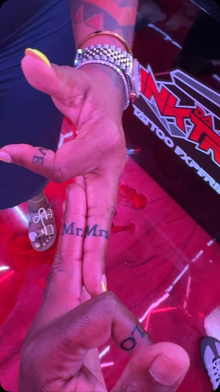 Two hands with matching Mr. and Mrs. tattoos on their fingers.