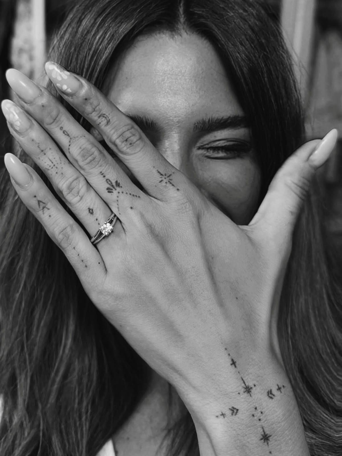 Hand with small geometric finger and wrist tattoos covering a person's face.