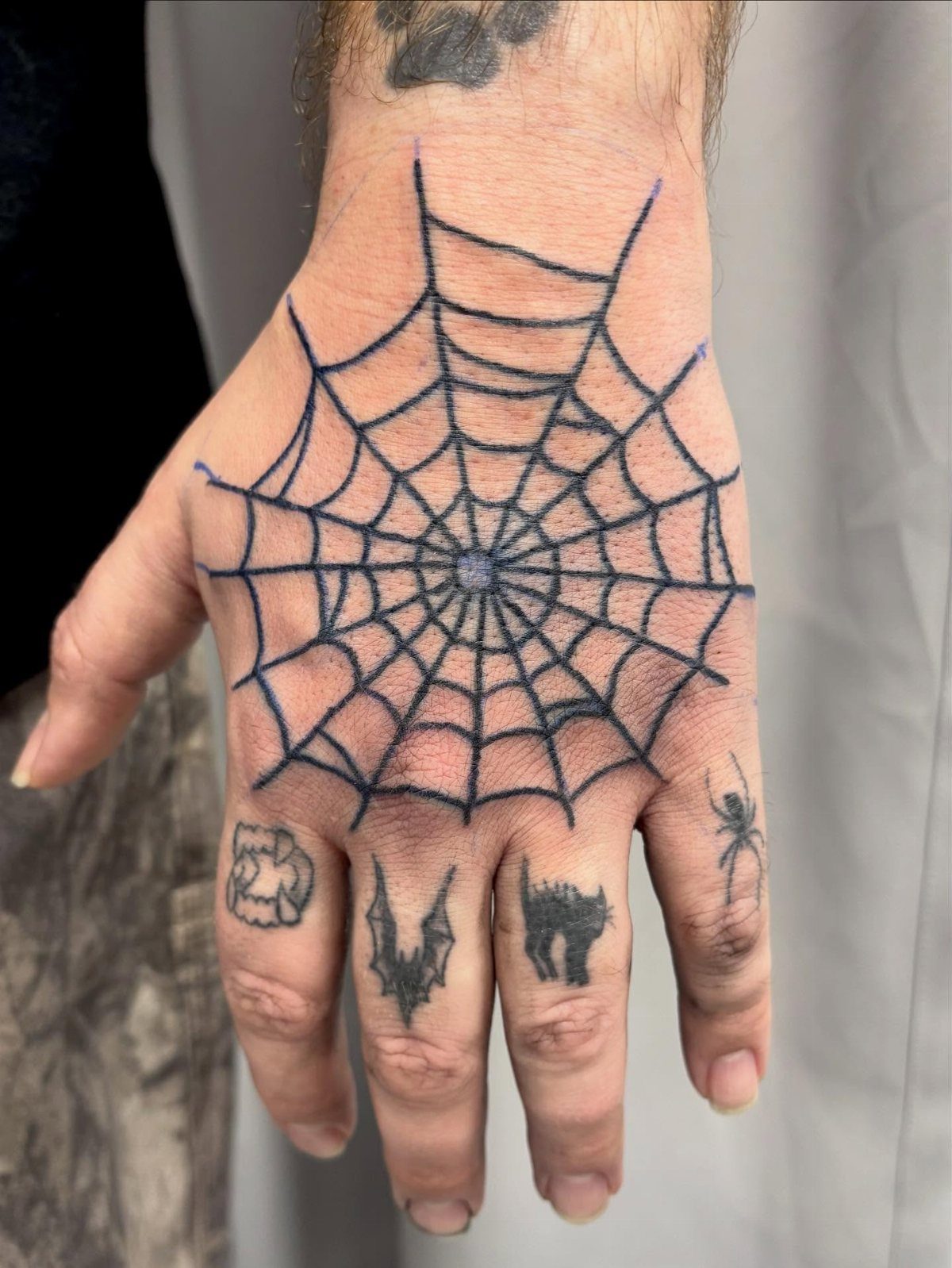 Hand and fingers with a large spider web tattoo and small spooky finger tattoos.