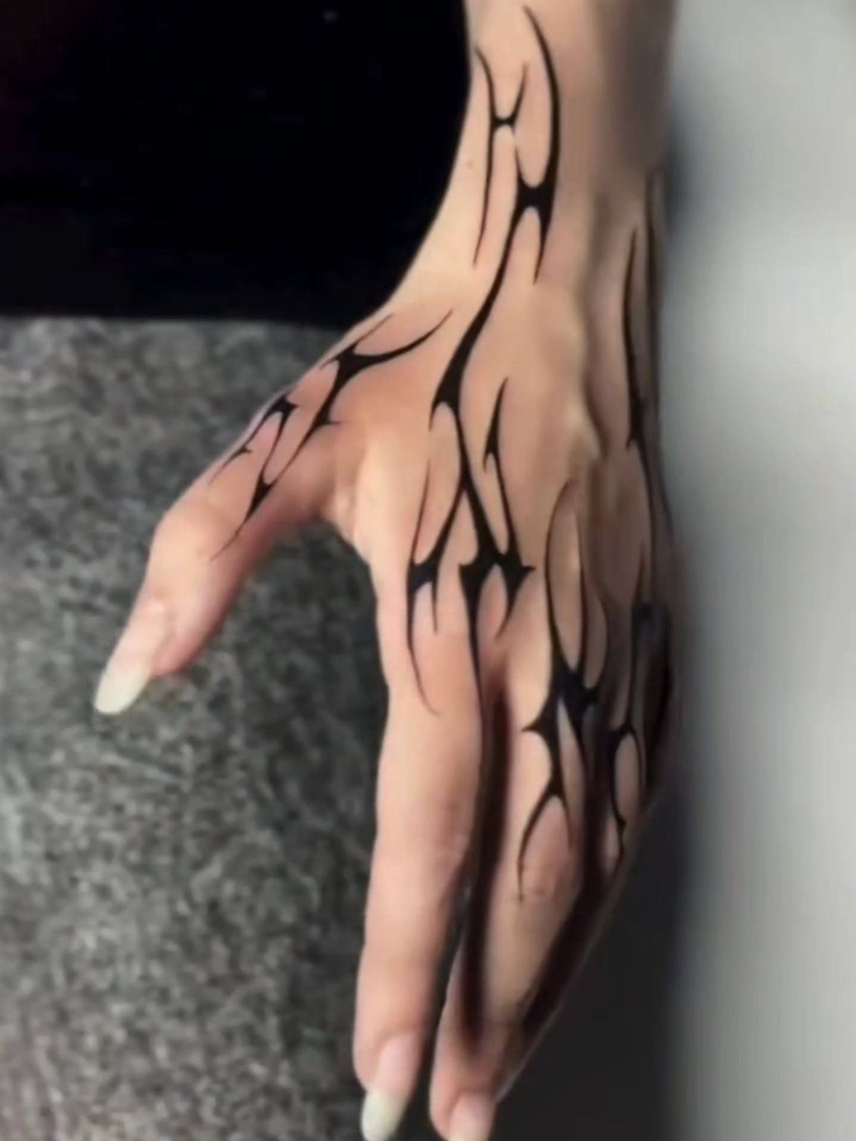 Hand with bold black tribal tattoos featuring sharp, flowing organic lines.