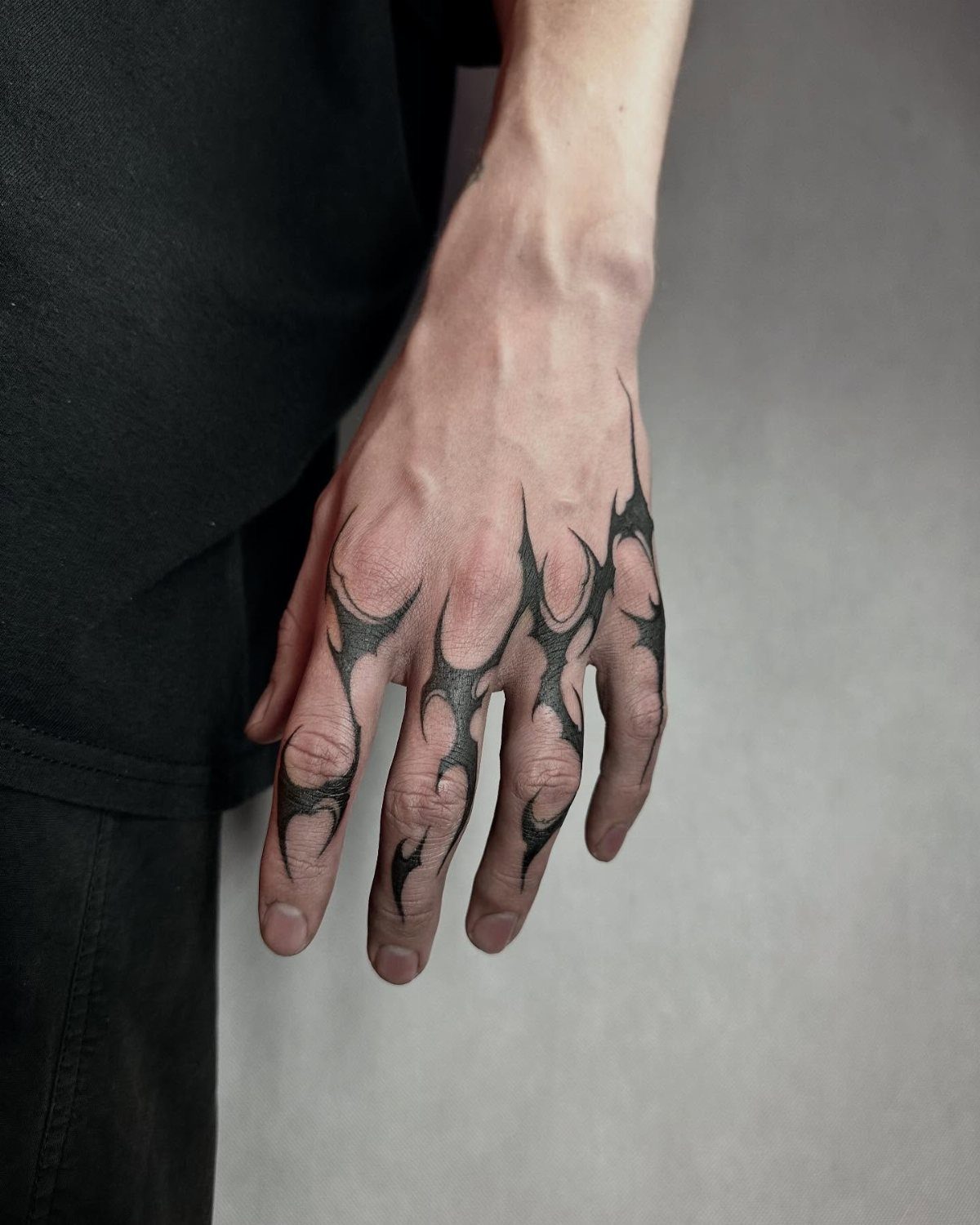 Hand with black thorn-like tattoos extending across knuckles and between the fingers.