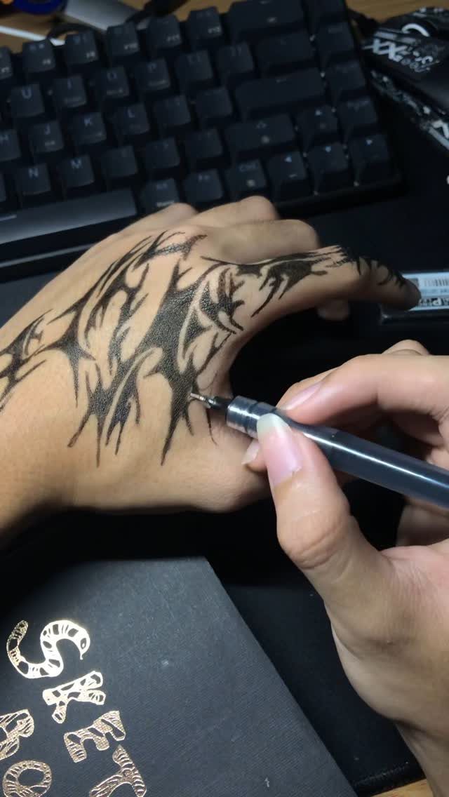 Hand with black ink abstract drawings being detailed with a fine-liner pen.