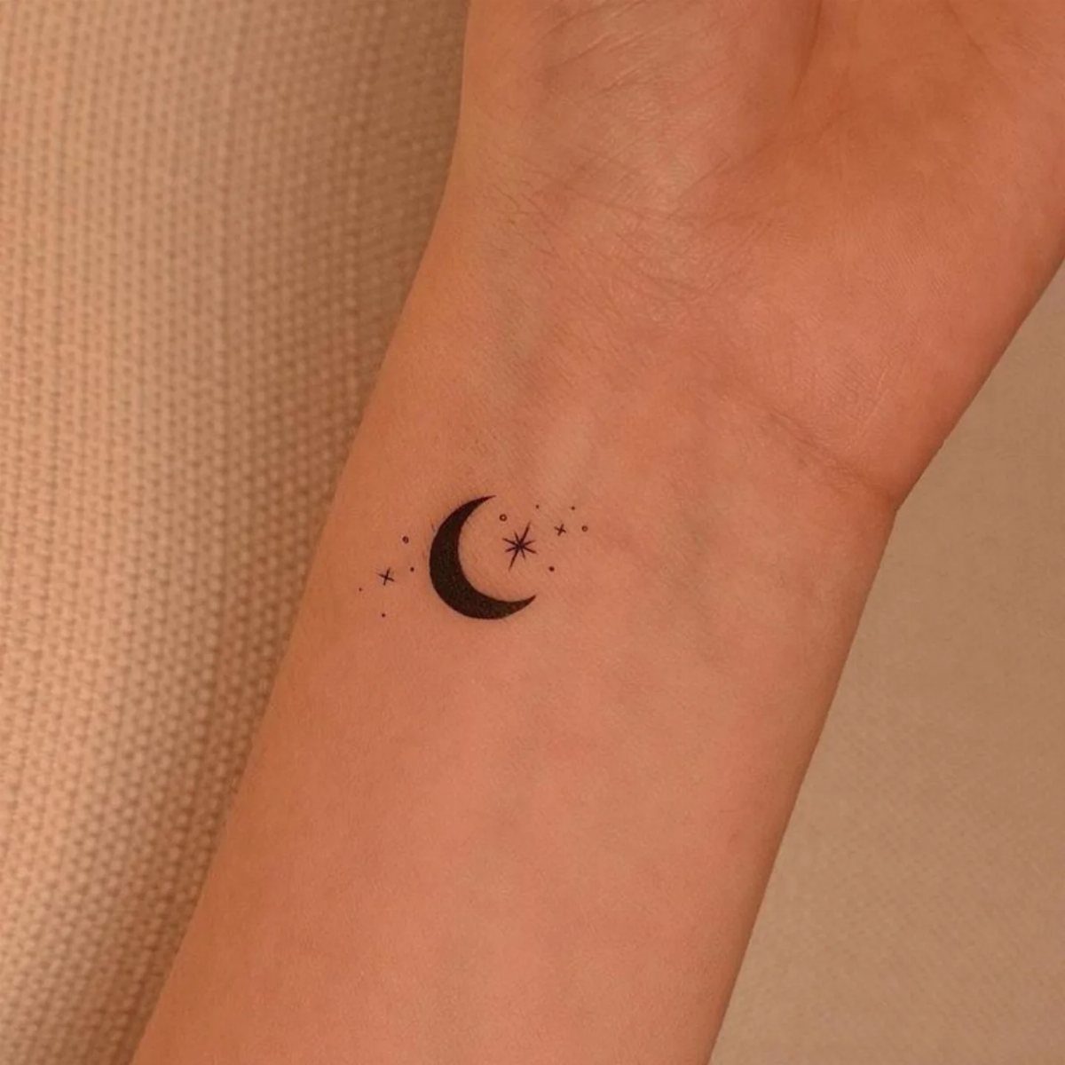 Crescent moon and stars tattoo in black ink on a person's wrist.