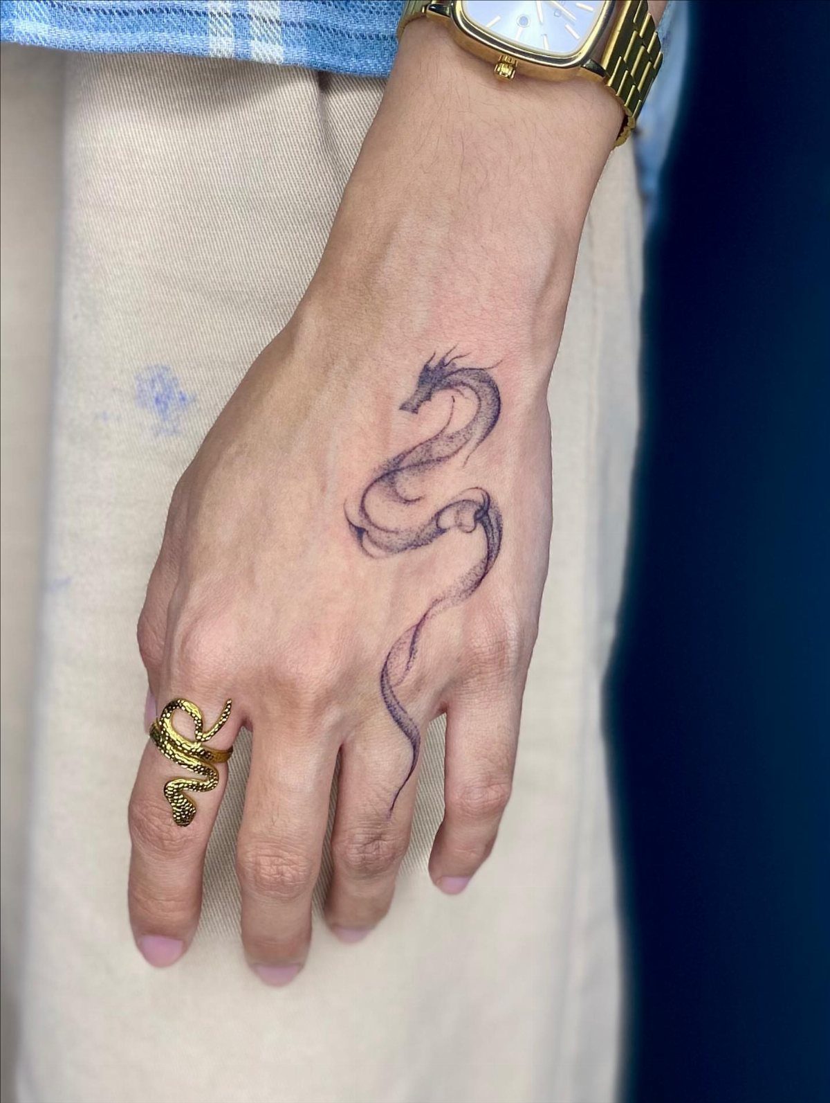 Dragon tattoo on the back of a hand with a gold dragon ring.