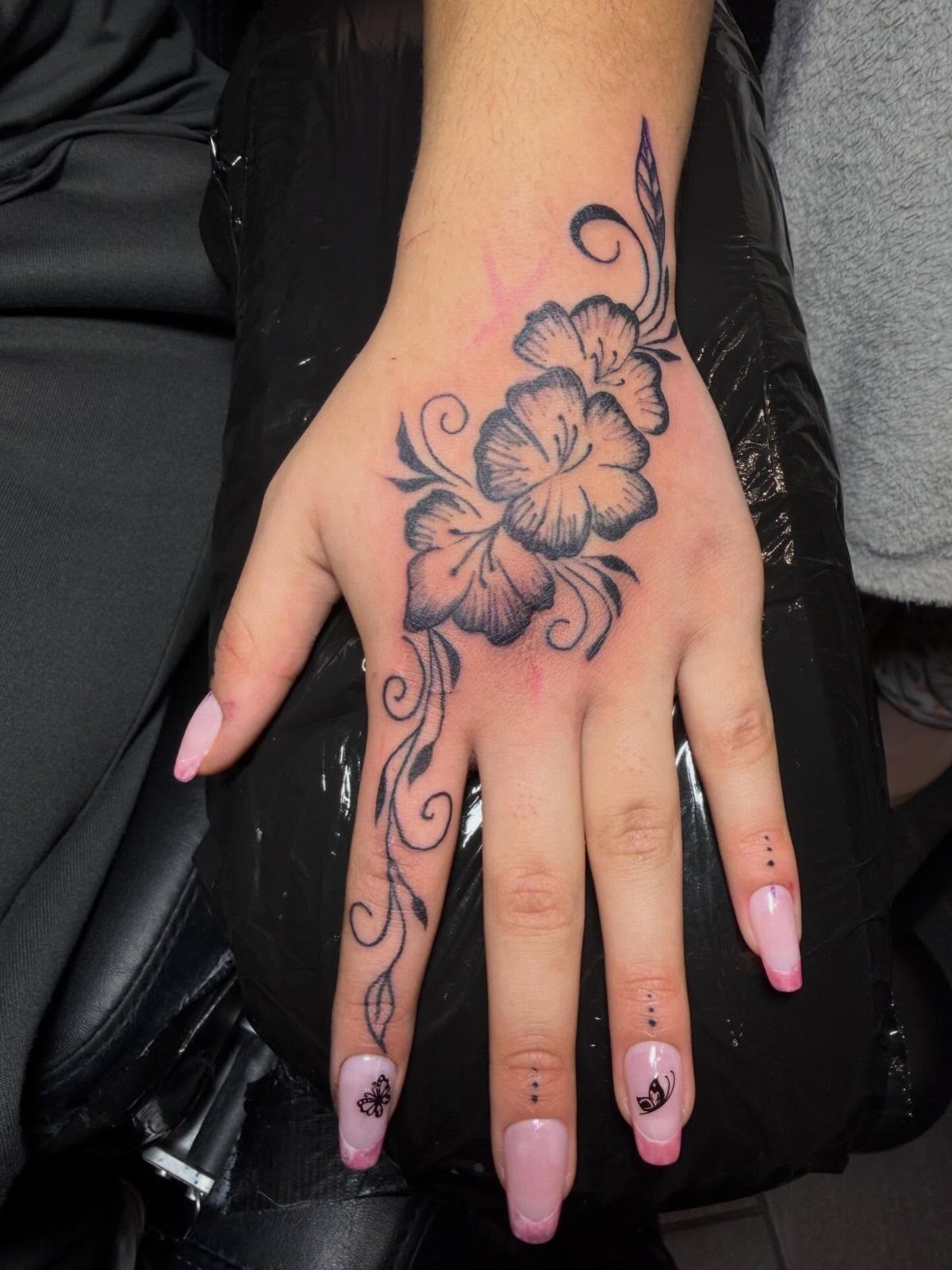 Hand with a black ink tattoo of flowers and swirling vines on the skin.