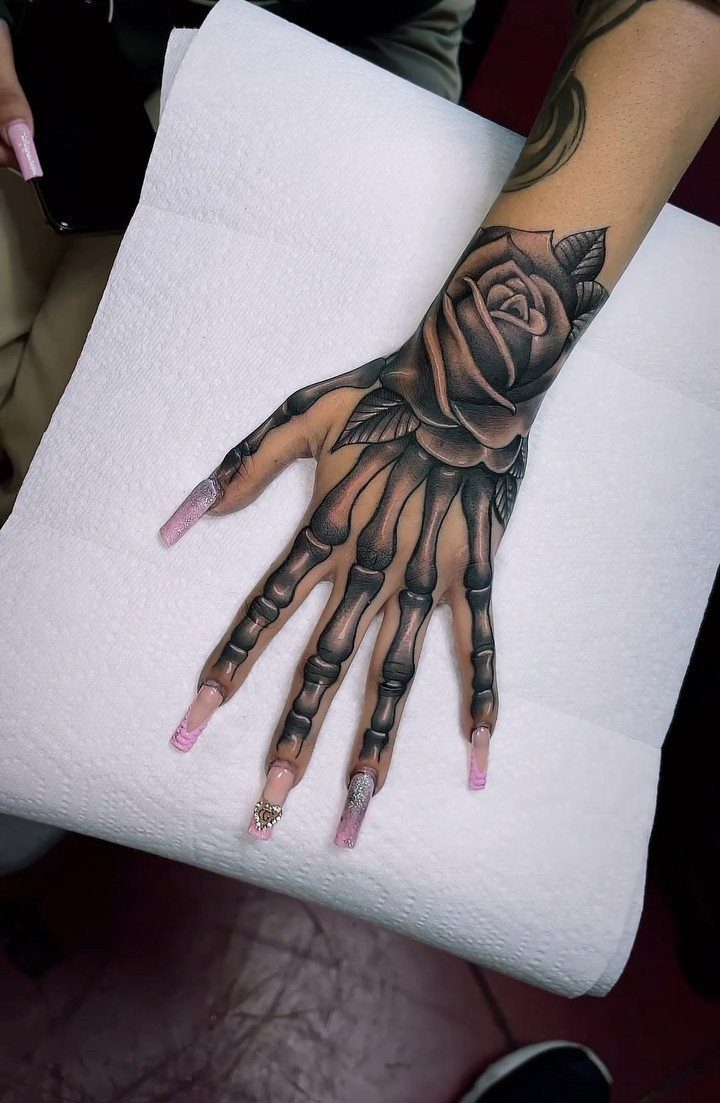 Skeletal finger bone tattoo merging with a large rose on a person's hand