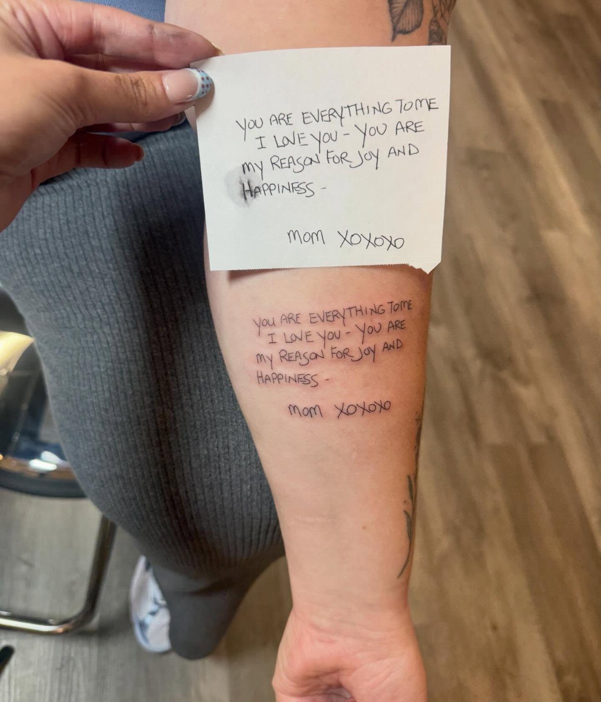Forearm with a text tattoo matching a handwritten note held above it.