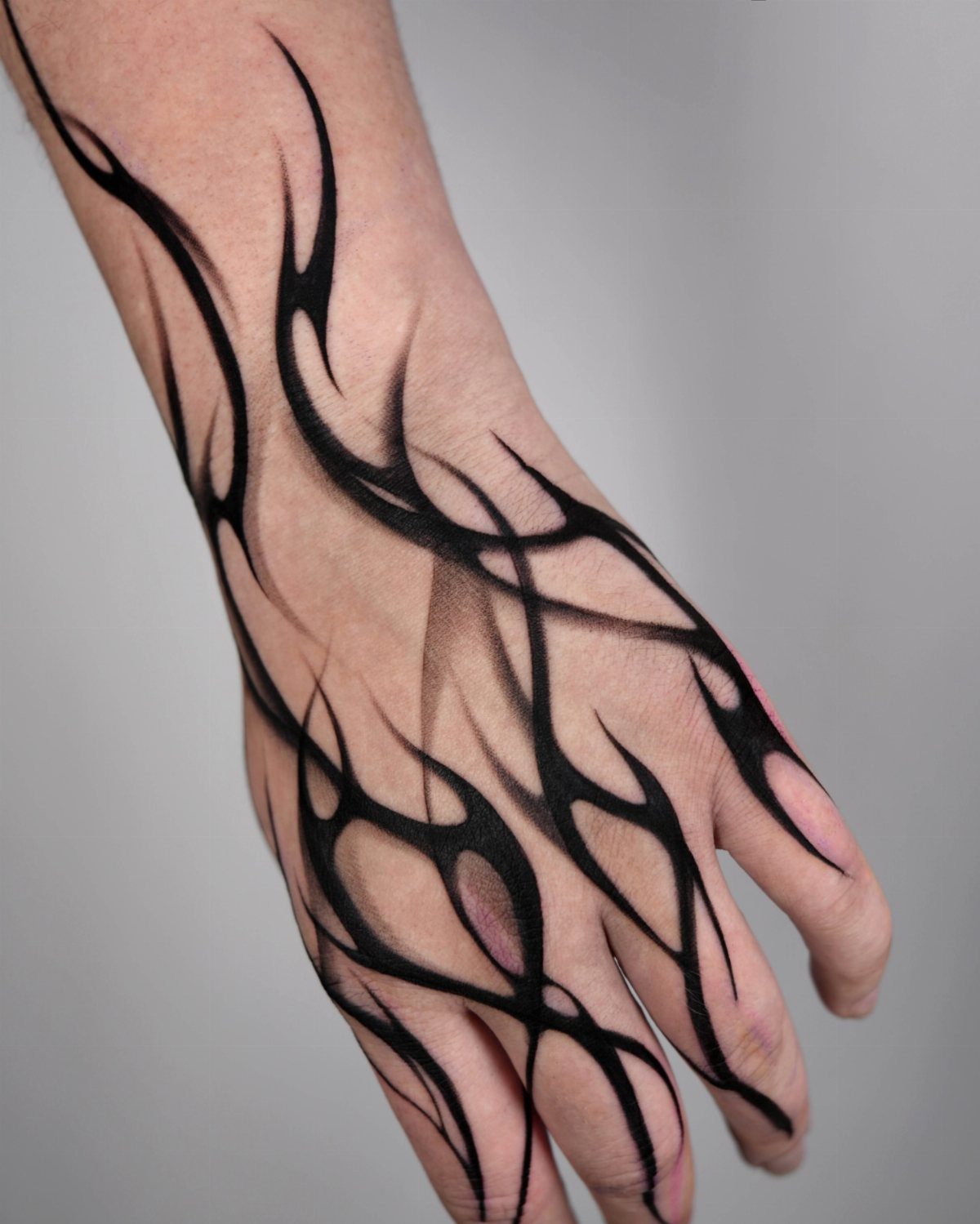 15 Hand Pen Tattoo Ideas for Spider Webs, Flowers and More 13 Hand and wrist with black ink tribal tattoos in sharp flame-like patterns.