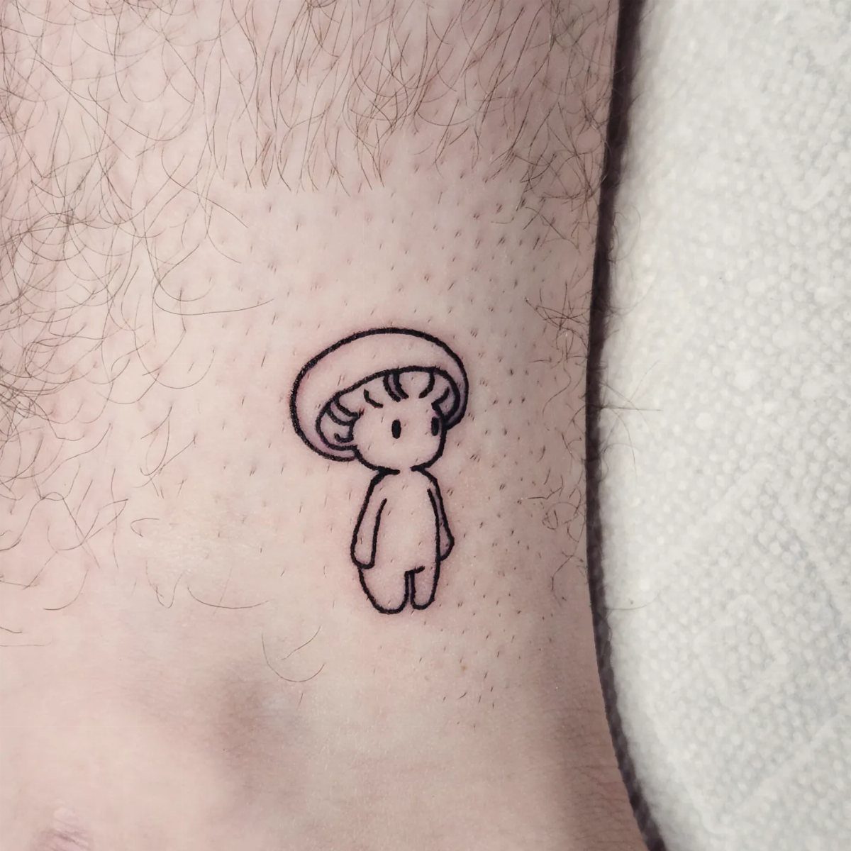 15 Hand Pen Tattoo Ideas for Spider Webs, Flowers and More 14 Small black ink tattoo of a cute mushroom character on hairy skin