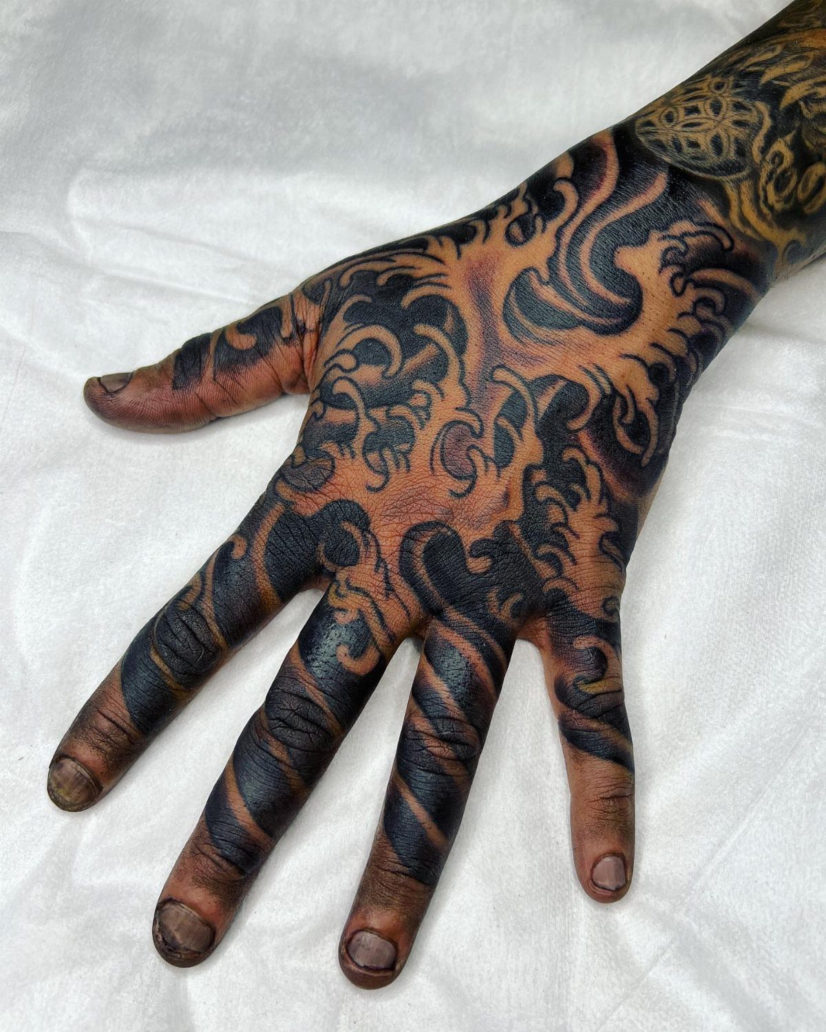 Tattooed hand with black and orange swirling abstract patterns on a white background