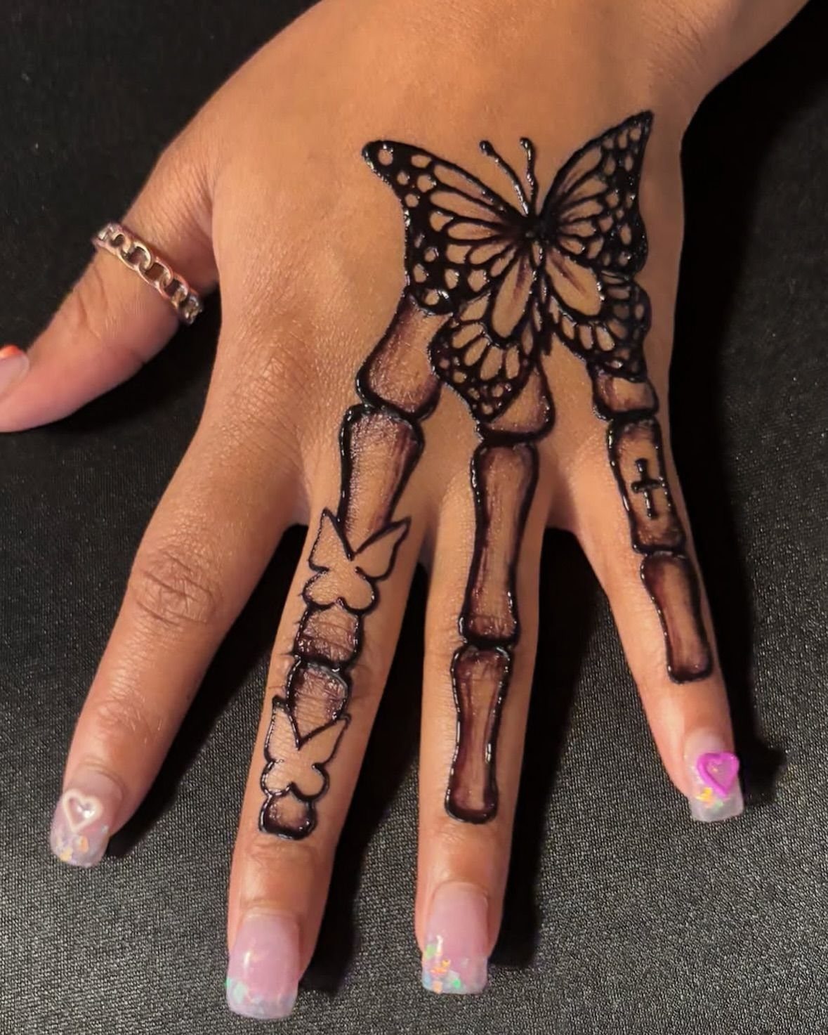 Hand with henna art featuring a butterfly and skeletal finger bone designs.